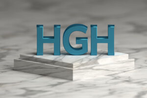 Bold blue letters HGH abbreviation of human growth hormone standing on marble pedestal.