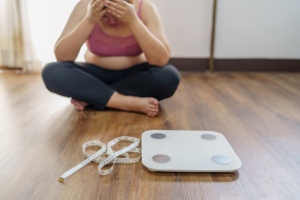 overweight woman with head in hands behind a scale